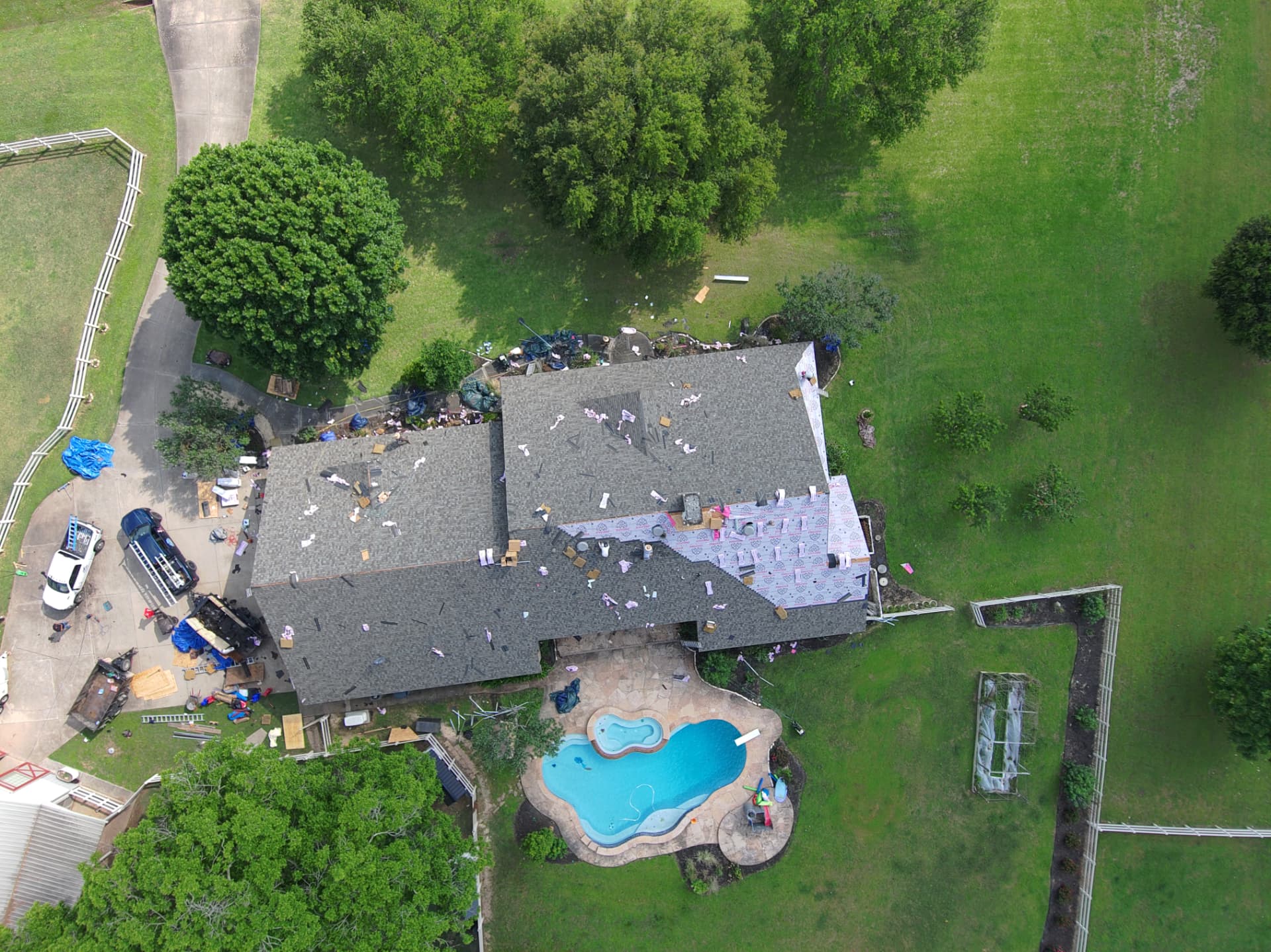 Aerial drone photo of a roof replacement underway on an acreage home with pool and equipment staged