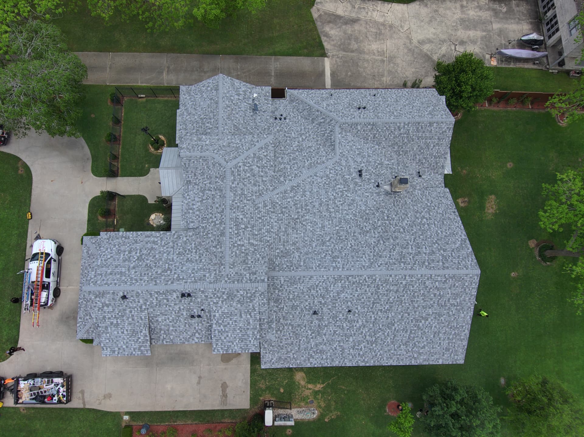 Top-down drone view of a completed light gray architectural shingle roof on a large Texas home